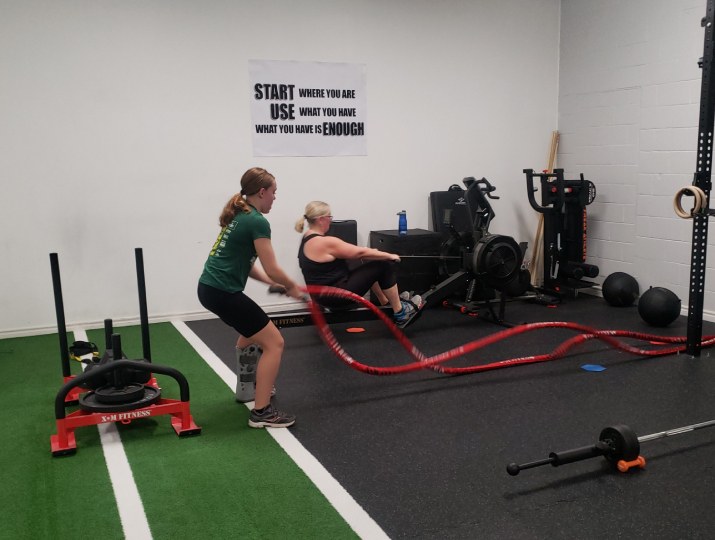A client training with battle ropes at Built by Faith Love Fitness, with the studio's Start Where You Are sign on the wall